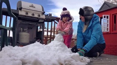 mother and daughter are bundled up outside building snowman. DENVER
