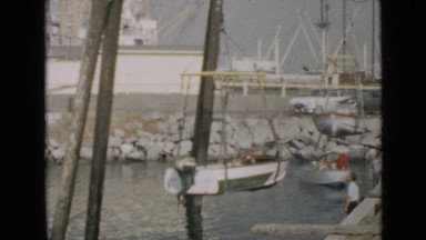 1953: boat being transported from land to sea with help of crane and two people