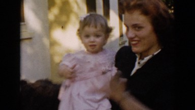 1953: mother helps toddler wave to camera, black dog in background CALIFORNIA
