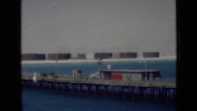 1947: pier or bridge over blue waterway with industrial plant in background
