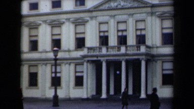 1946: on rainy day, cars and pedestrians pass buildings and statue