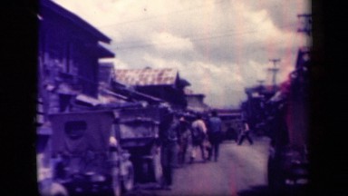 1944: military jeeps and personnel traveling down dirt road in ramshackle town.