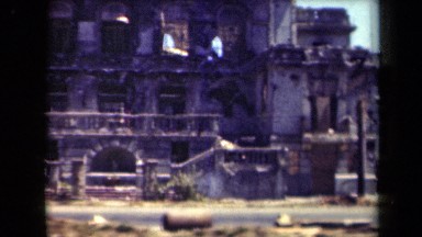 1944: old type of building located alone and some cars are moving in front.