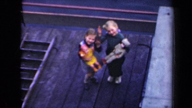 1946: two children holding dolls on dock wave to camera NETHERLANDS