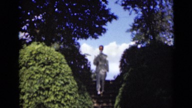 1947: Man in White Suit Coming Down Stairs Near Green Bushes