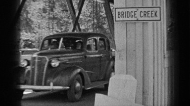 1937: desoto family car crosses covered bridge, sign reads "bridge creek."