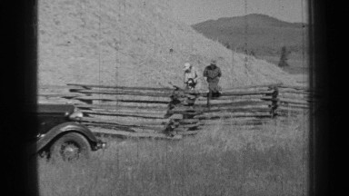 1937: two women sitting on wood fence let dog loose to run in open field.