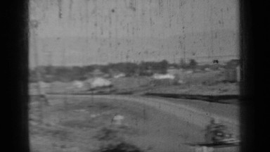 1937: people in front and back seats of car waving with large item