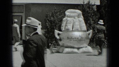 1937: man standing on ladder and repairing name board watched by others