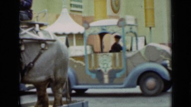 1937: man sitting atop elephant at colorful vehicle loaded with people