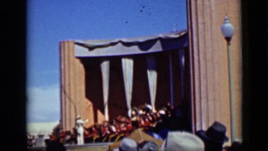 1937: band plays in outdoor arena filled with spectators on sunny day