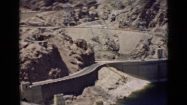 1939: sweeping view of large, historic hoover dam, cars driving by in background