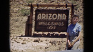 1939: woman poses by hanging wooden sign containing greeting and location