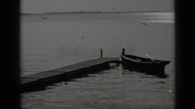1939: older woman sits at end of pier and man walks along pier by child