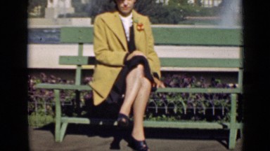 1939: woman in brown coat sitting on wooden bench cross legged SAN FRANCISCO
