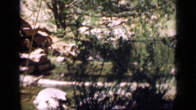 1939: woman standing on rustic log bridge at base of rocky butte. UTAH
