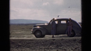 1939: three people standing around classic parked car, having conversation
