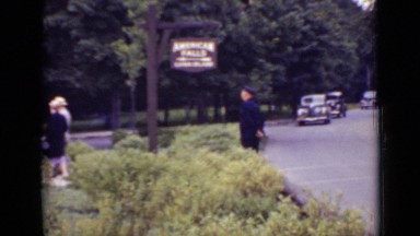 1940: cars driving by park where guard is standing and people are walking around
