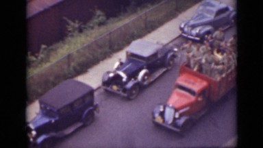 1940: red automobile drives group of men passed parked cars near niagara falls.