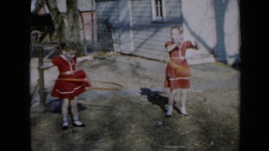 1958: two girls in red dresses having fun playing with hula hoops outside
