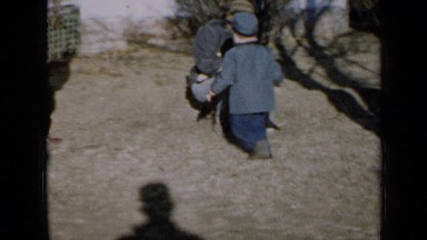 1958: child runs behind men who is playing with pet dog and men who is watching