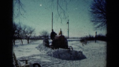 1958: man plows snow-covered farm with tractor and then he feeds his dogs
