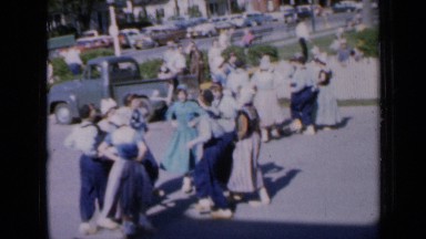 1959: women dancing together in city alongside road while car traffic is going