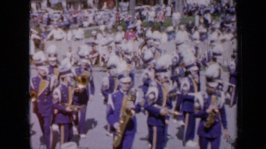 1959: marching band in blue uniforms with instruments during town parade IOWA
