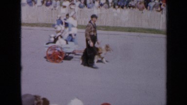 1959: people of all ages along roadside watching small procession of others.