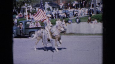 1959: well dressed cowboy riding horse down street while carrying flag IOWA