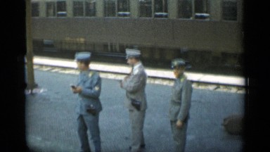 1962: three uniformed men standing by railroad track, one of them smoking MONACO