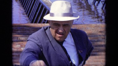 1971: an old man in blue sport coat and white cap looks around, critically.