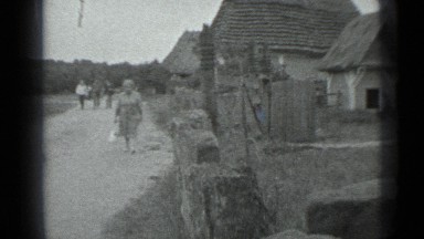 1983: older woman and three younger people walk on country lane past houses