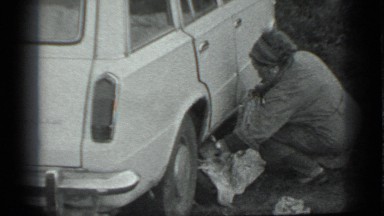 1983: woman kneeling down beside car, covering something with blanket RUSSIA