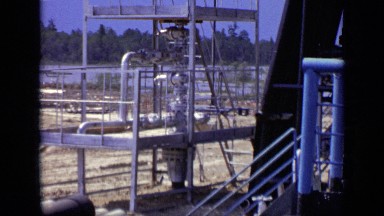 1971: natural gas wellhead stands amid piping while man stands near two drills