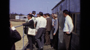 1971: photographer outside taking pictures of group of men as they inspect
