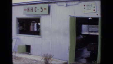 1971: people engaged in talking, walking etc, near to white painted building