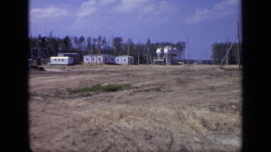 1971: road and widespread land with people's walking around and trees and house