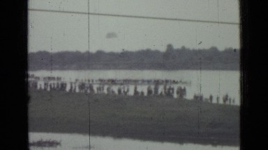 1967: people line shore and pier to watch parachutists land in front of them