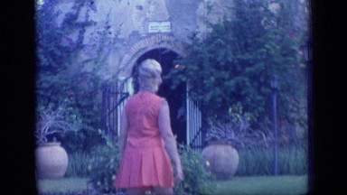 1970: woman in dress stands in front of old castle-like building. PUERTO RICO