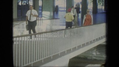 1970: woman wearing sunglasses points over metal railing to level below PUERTO