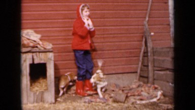 1964: child in red coat and boots plays with two puppies KANSAS