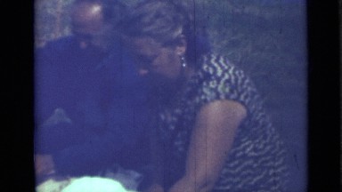 1967: family of three sitting outside on grass, enjoying nice picnic together.