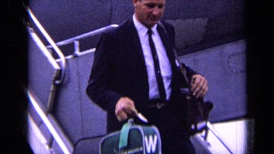 1963: men in black suit coming down stairs from airliner while carrying bags