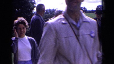 1963: few men review papers by flower bed in garden as people walk by them