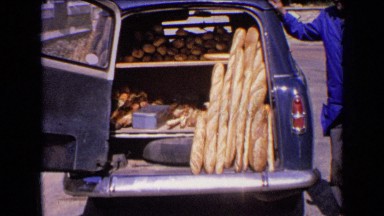 1963: Street Vendor Wearing Blue Shirt Standing Near Car with Food Items