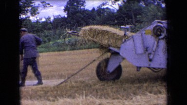 1963: man working in field, while tractor pulls hay. FRANCE