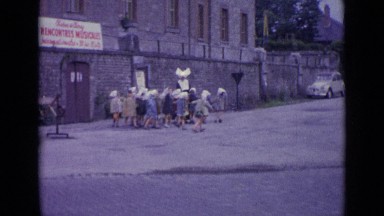 1962: little children's walking on street with women at side of building