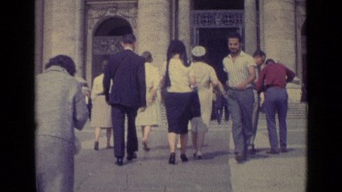 1962: crowd of people making their way towards building. one man is hurrying