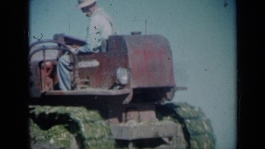 1961: man in red tractor backing up into pile of grass. MISSOURI
